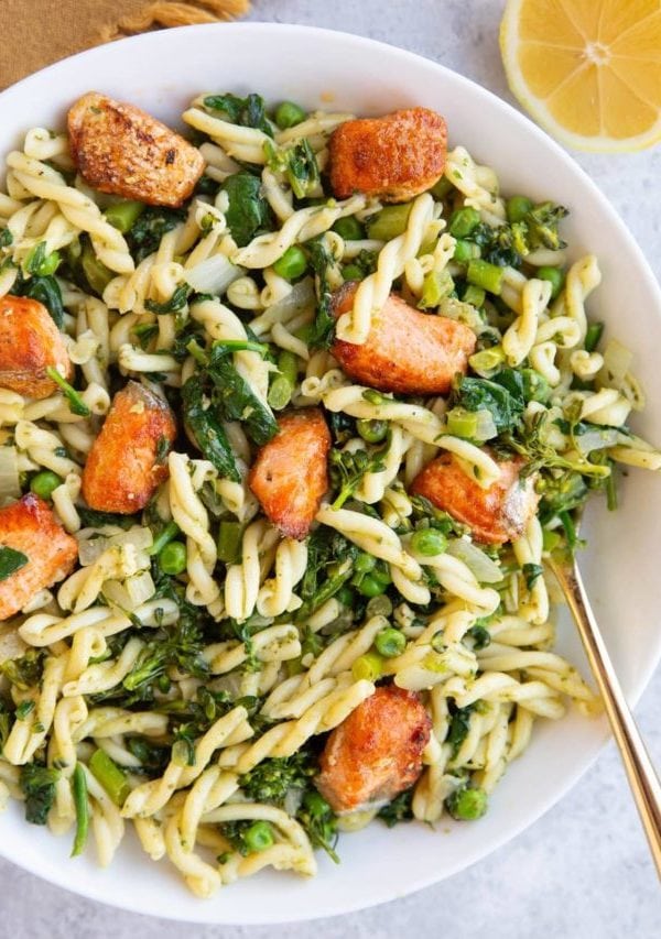 Large white bowl full of pesto pasta with salmon on top.