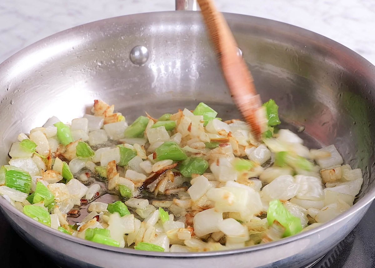 Stainless steel skillet cooking onion, celery, and garlic.