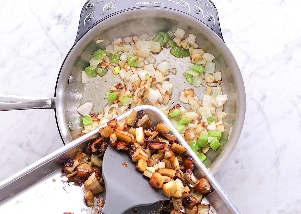 Pouring roasted eggplant into the skillet with the sauteed onion and celery.
