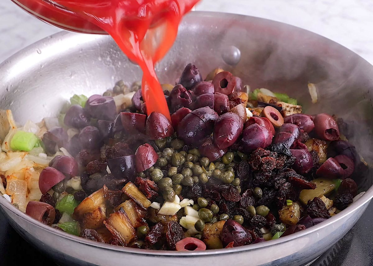 Pouring the rest of the caponata ingredients into the skillet.