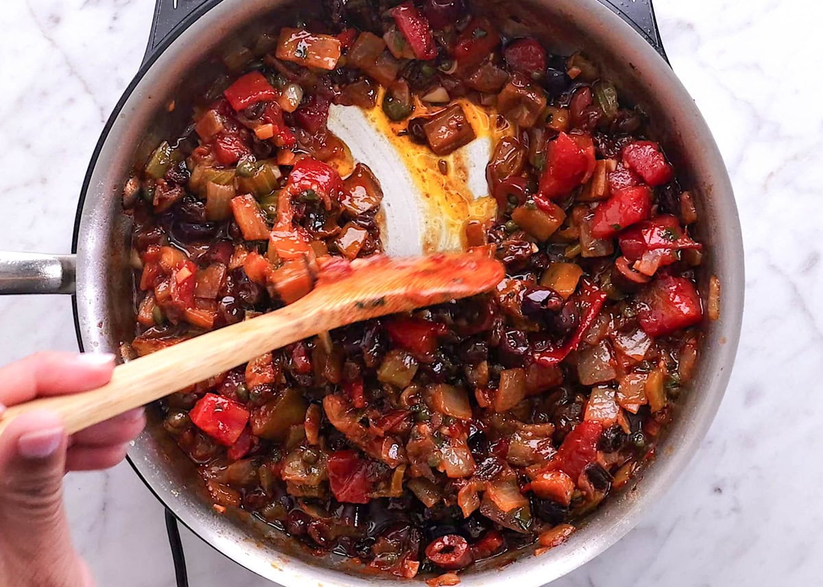 Hand holding a wooden spoon stirring homemade caponata.