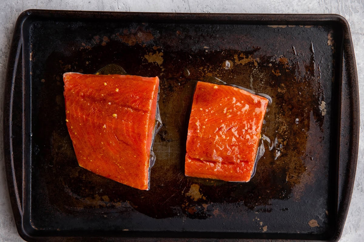 Two salmon filets on a baking sheet in a spice mixture marinade.