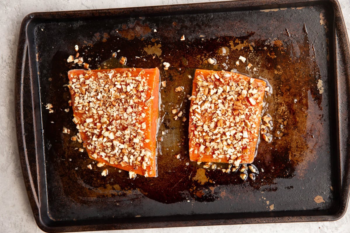 Salmon filets with pecans on top on a baking sheet, ready to go into the oven.