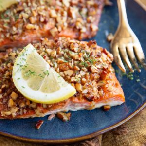 Pecan encrusted salmon filets on a plate with a golden fork and slices of lemon, ready to serve.