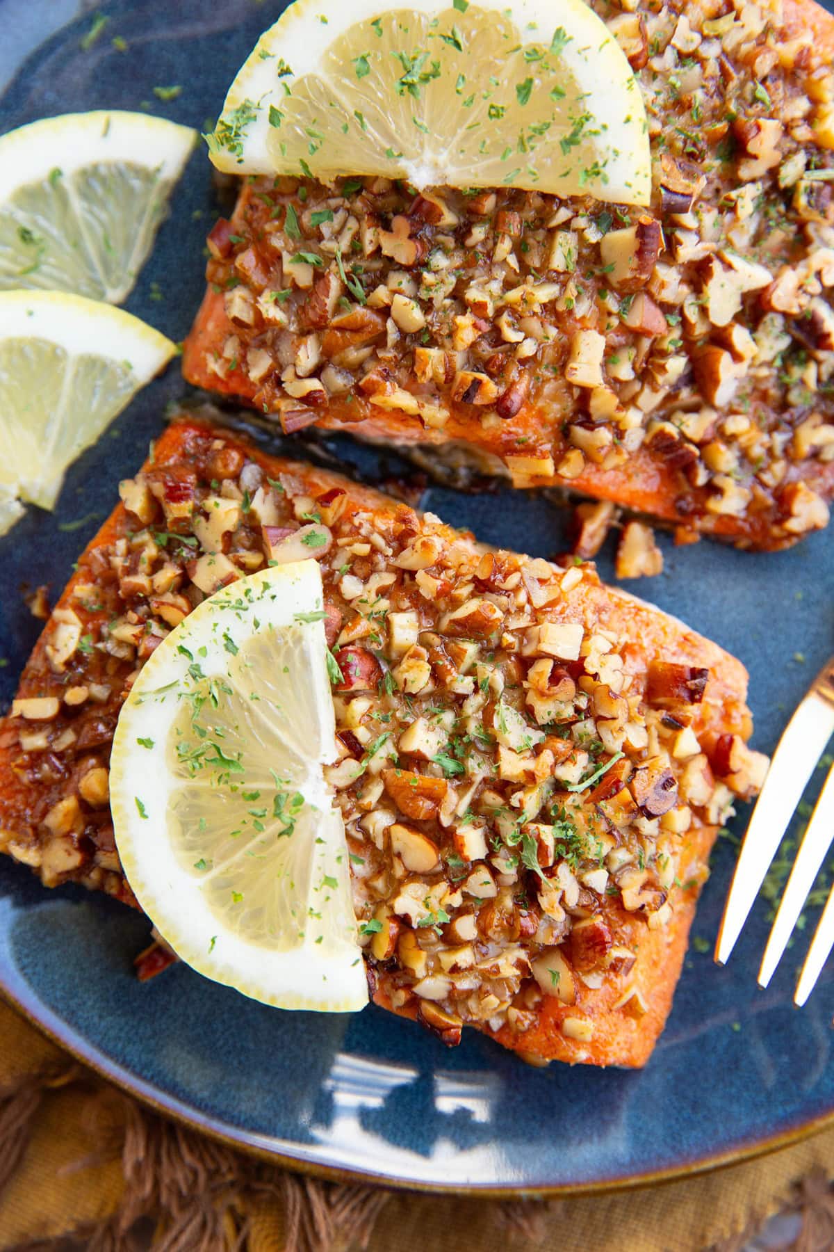 Two pecan crusted salmon fillets on a blue plate with slices of lemon.