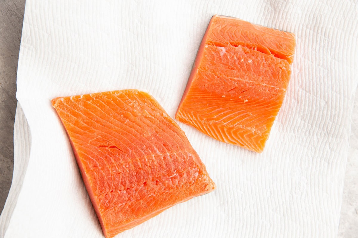 Two salmon fillets on a plate on a paper towel.