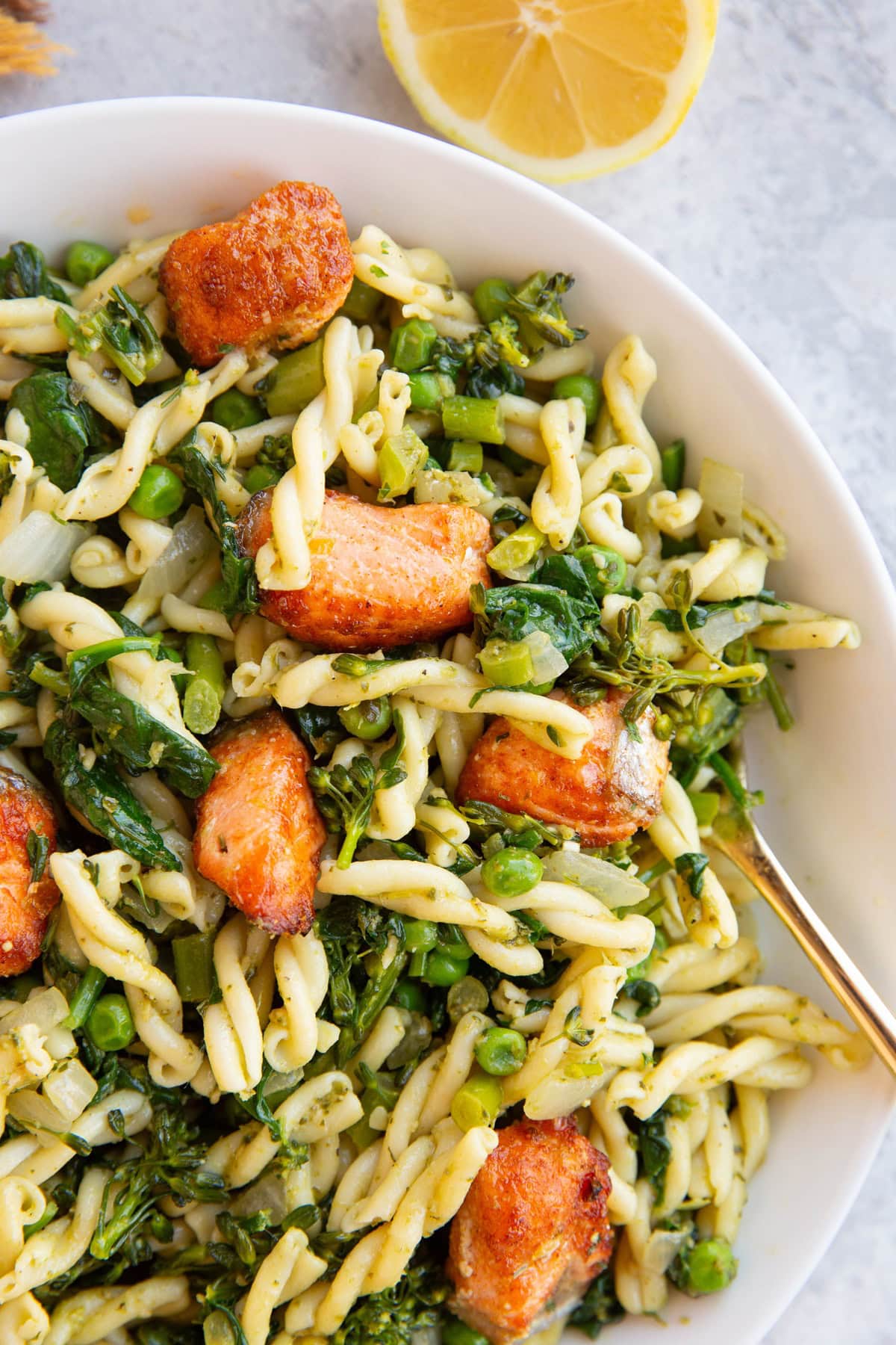 Large bowl full of salmon pesto pasta with a fresh lemon to the side.