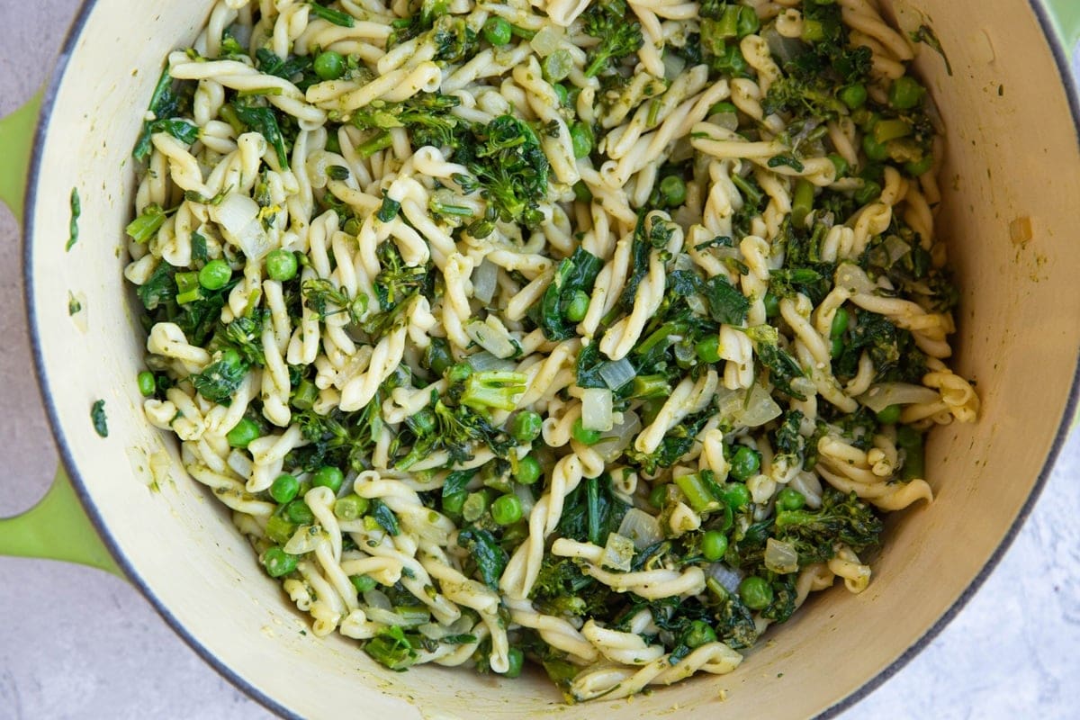 large pot full of pesto pasta with broccoli, spinach, and peas.