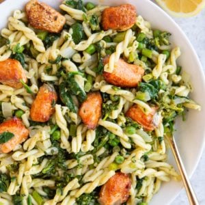 Large white bowl full of pesto pasta with salmon on top.