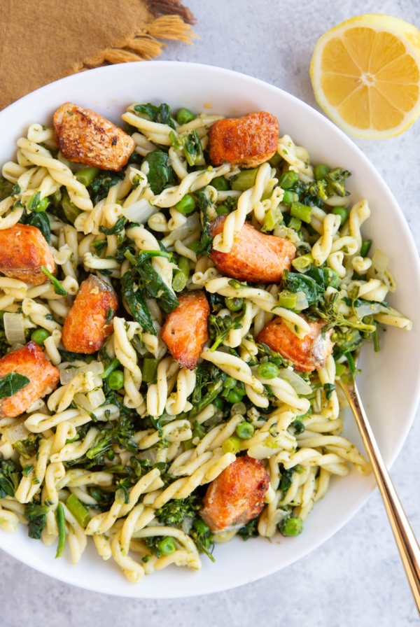 Large white bowl full of pesto pasta with salmon on top.
