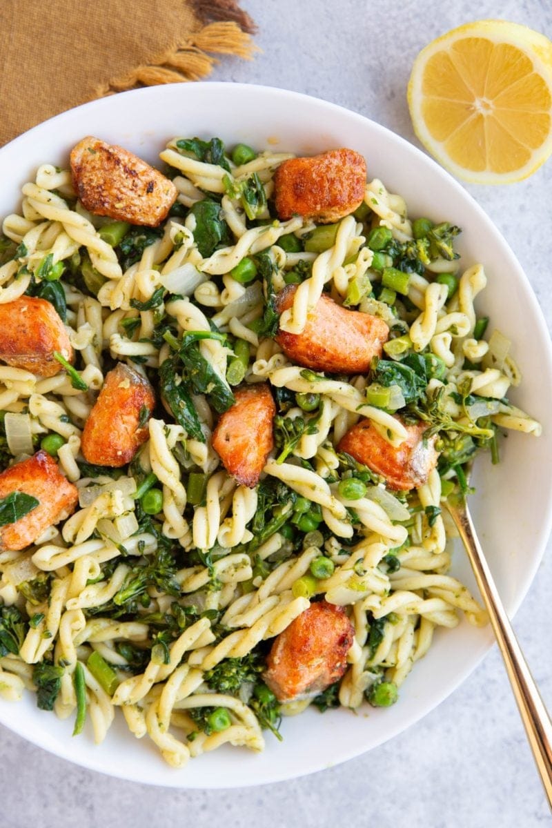 Large white bowl full of pesto pasta with salmon on top.