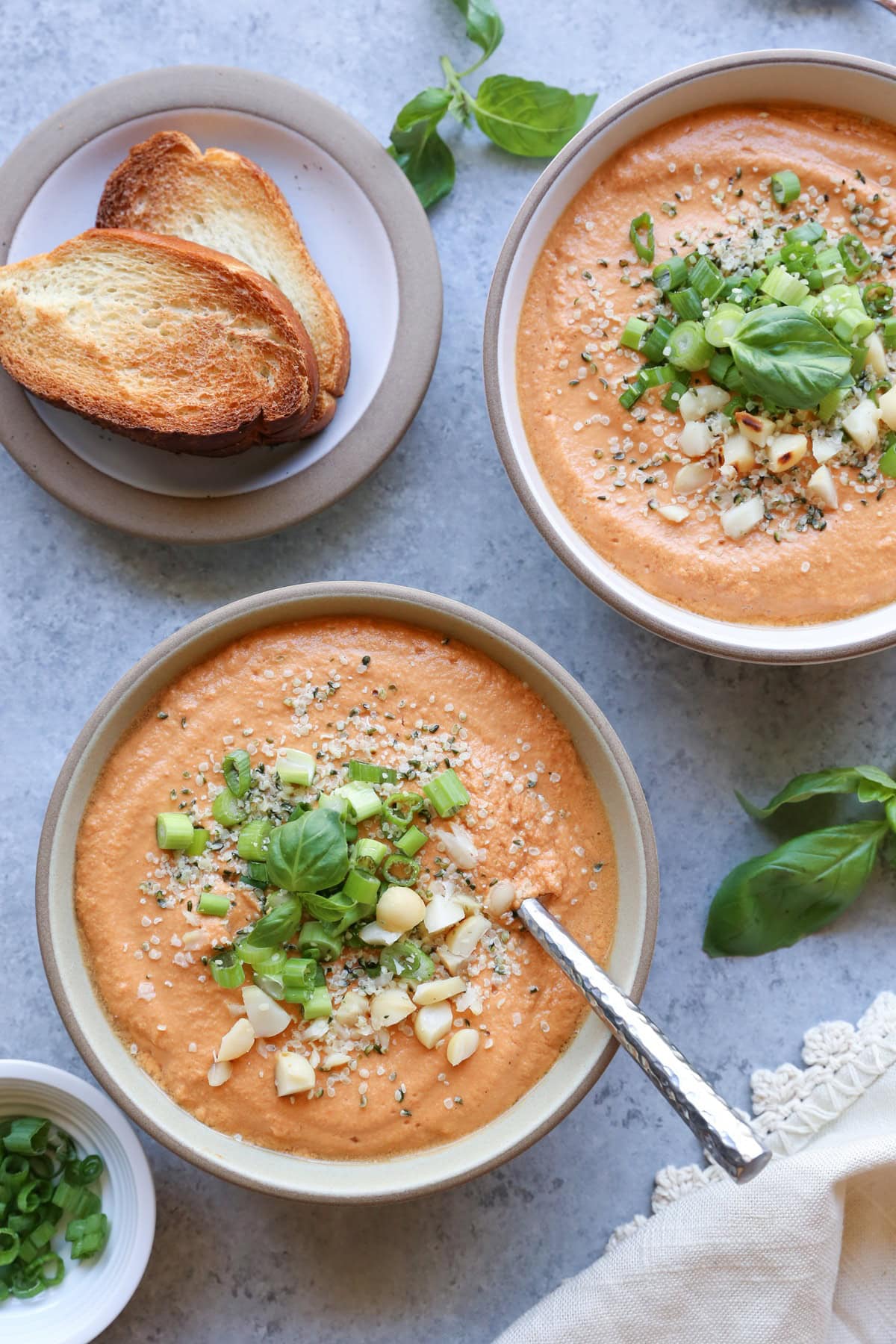 Two bowls of tomato soup with goodies sprinkled on top and toasted bread to the side.