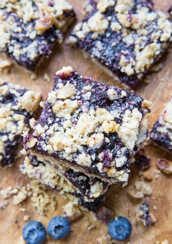 Pile of blueberry crumb bars on a wooden cutting board.