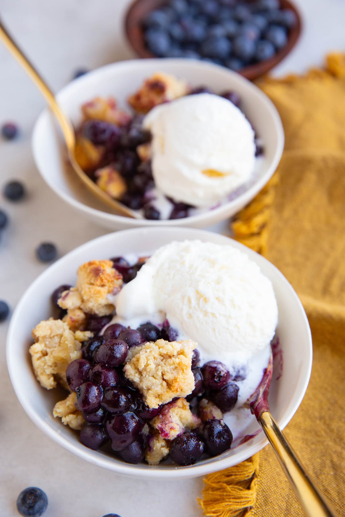 Two bowls full of blueberry crumble with scoops of vanilla ice cream on top.
