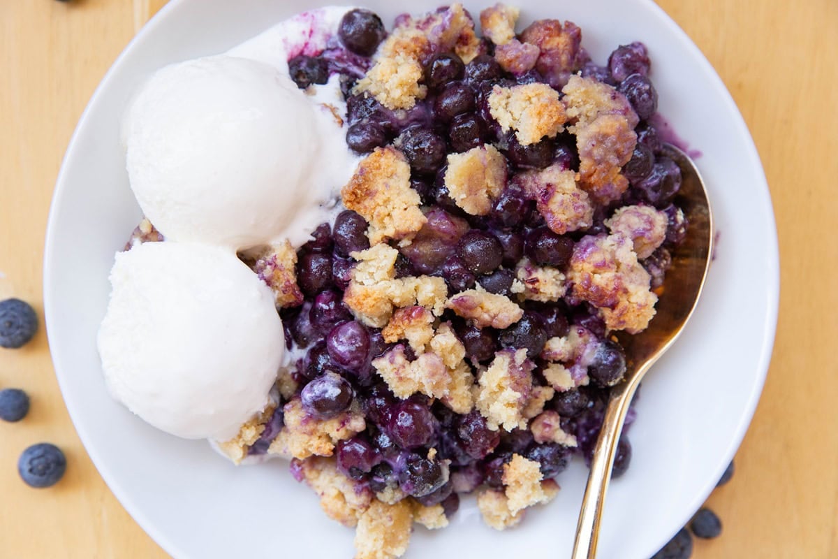 Blueberry crumble in a bowl with two scoops of vanilla ice cream, ready to serve.