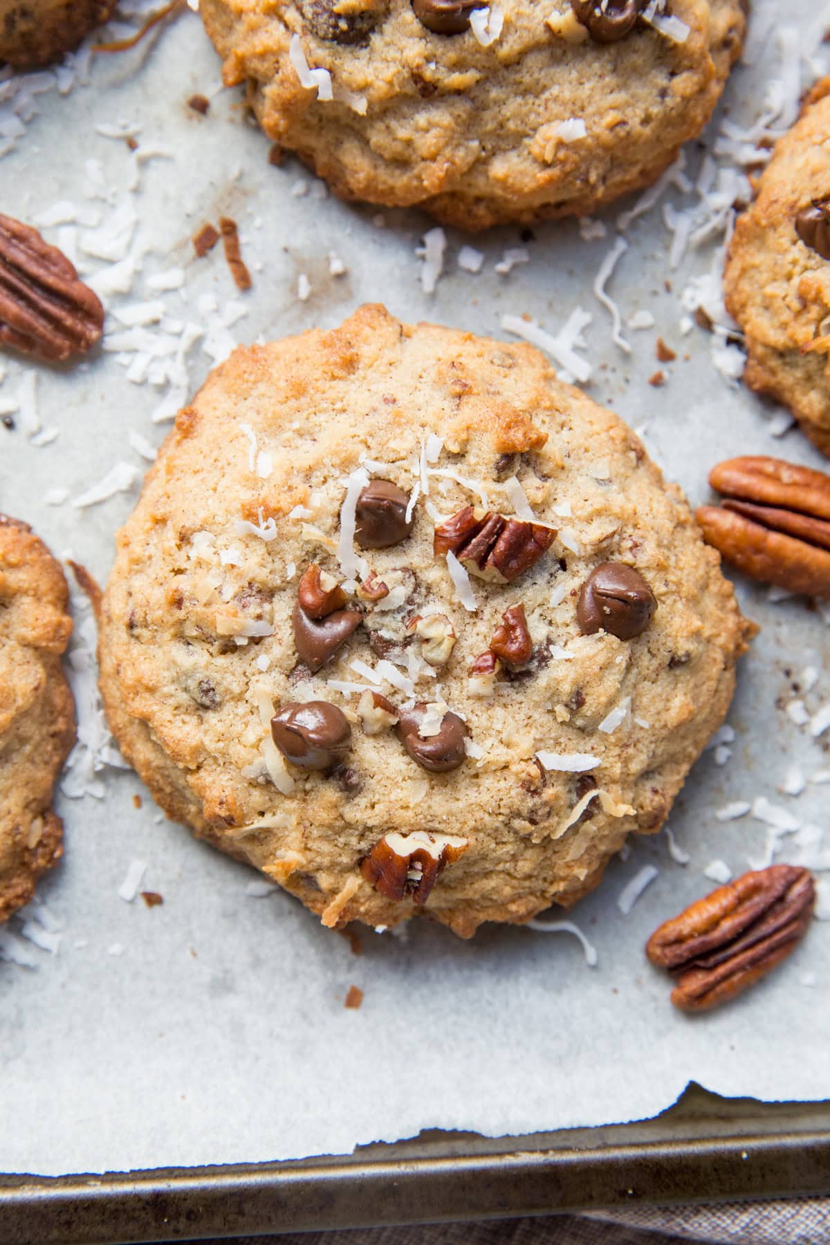 Cookies on a cookie sheet with pecans, chocolate chips, and shredded coconut.
