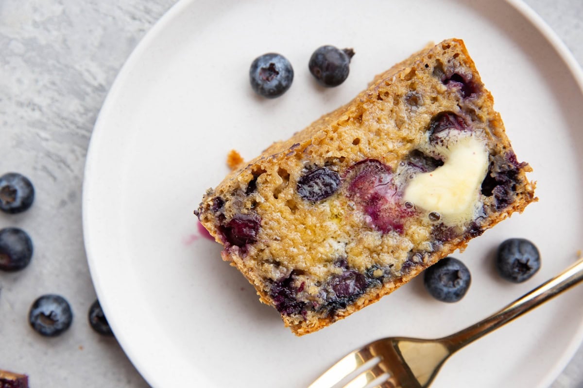 Thick slice of blueberry bread on a plate with melted butter on top.