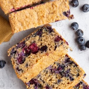 Loaf of blueberry bread, cut into sliced with fresh blueberries all around.