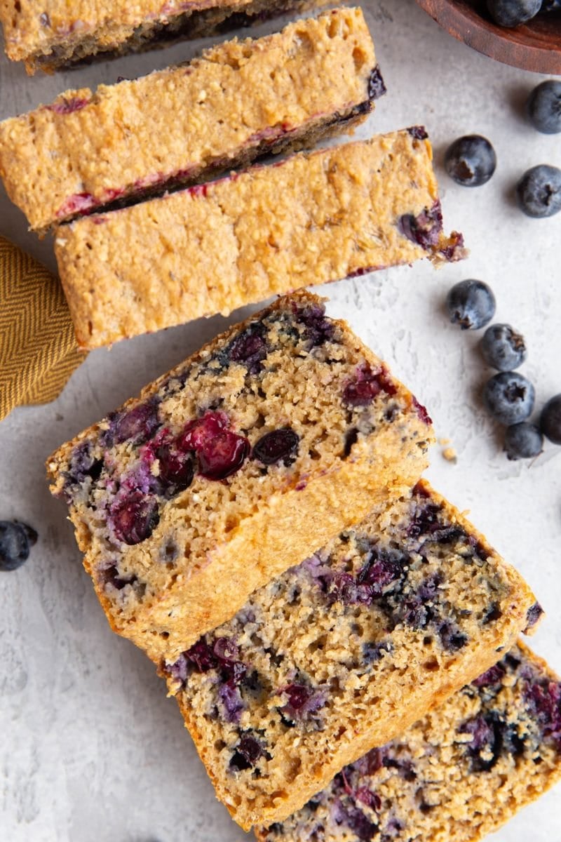 Loaf of blueberry bread, cut into sliced with fresh blueberries all around.