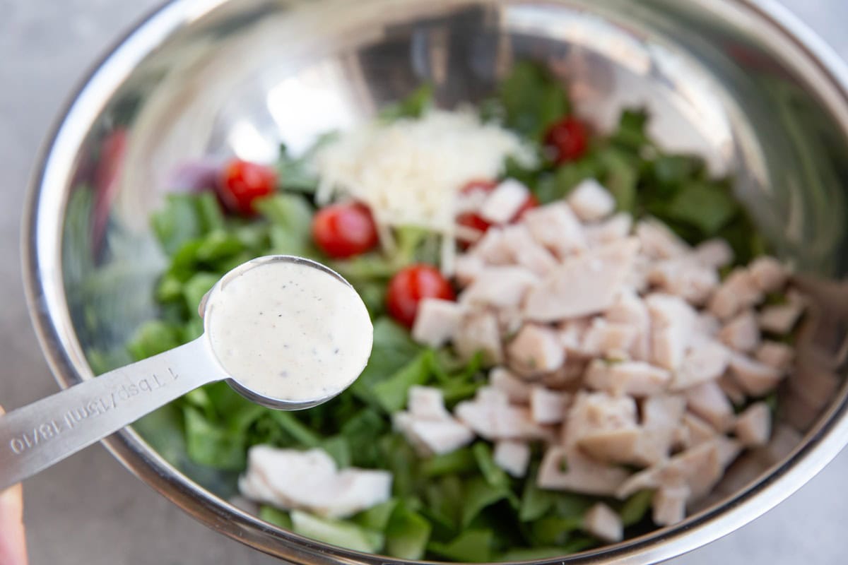 Holding a tablespoon of dressing over the mixing bowl, ready to be added in.
