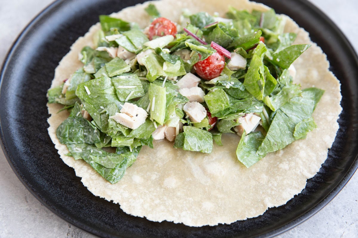 Tortilla on top of a plate with salad in the middle, ready to be turned into a wrap.