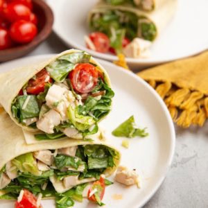 Chicken Caesar Wraps cut in half on a plate to expose the inside. More wraps in the background.
