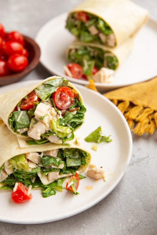 Chicken Caesar Wraps cut in half on a plate to expose the inside. More wraps in the background.
