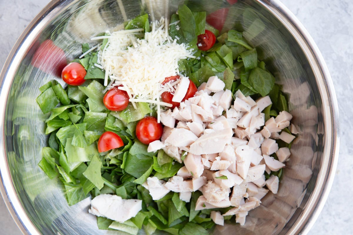 Mixing bowl full of chopped lettuce, chicken, tomatoes, and parmesan cheese.