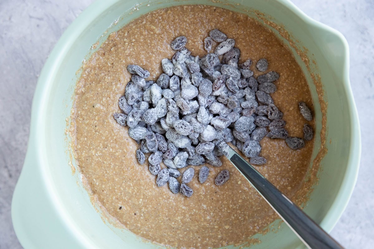 Mixing bowl with bread batter and floured raisins on top, ready to be mixed in.