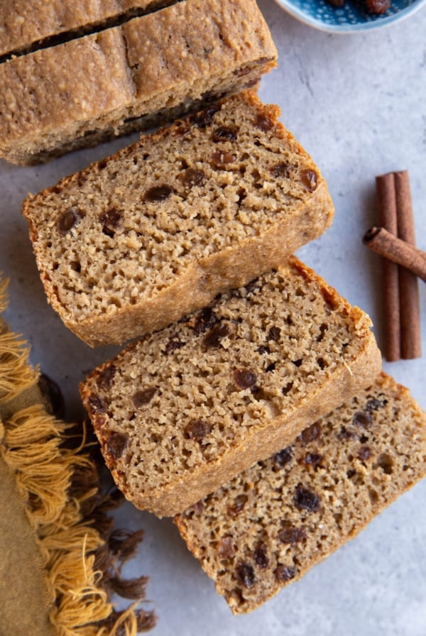 Loaf of cinnamon raisin bread cut into thick slices with cinnamon sticks to the side.