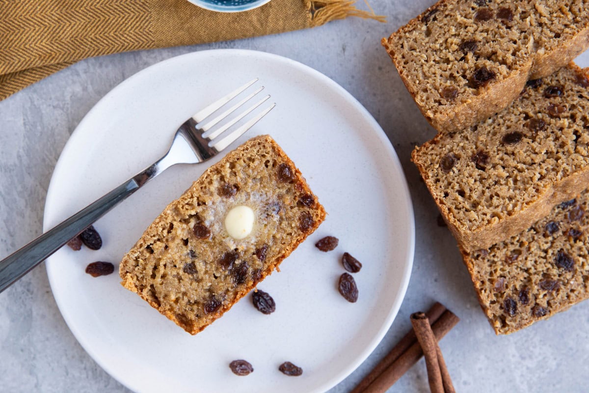 Plate with buttered cinnamon raisin bread with the rest of the loaf to the side.