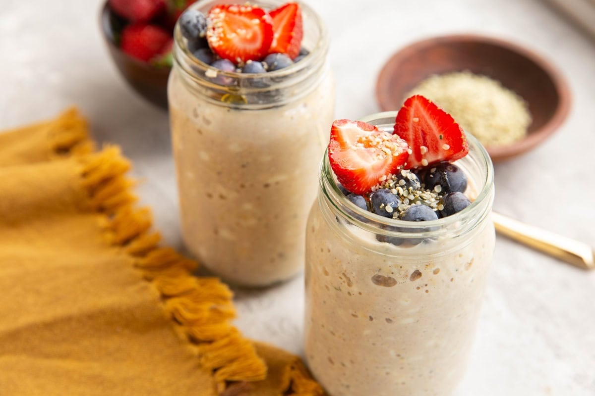 Two mason jars full of cottage cheese overnight oats with fresh berries and hemp seeds on top.