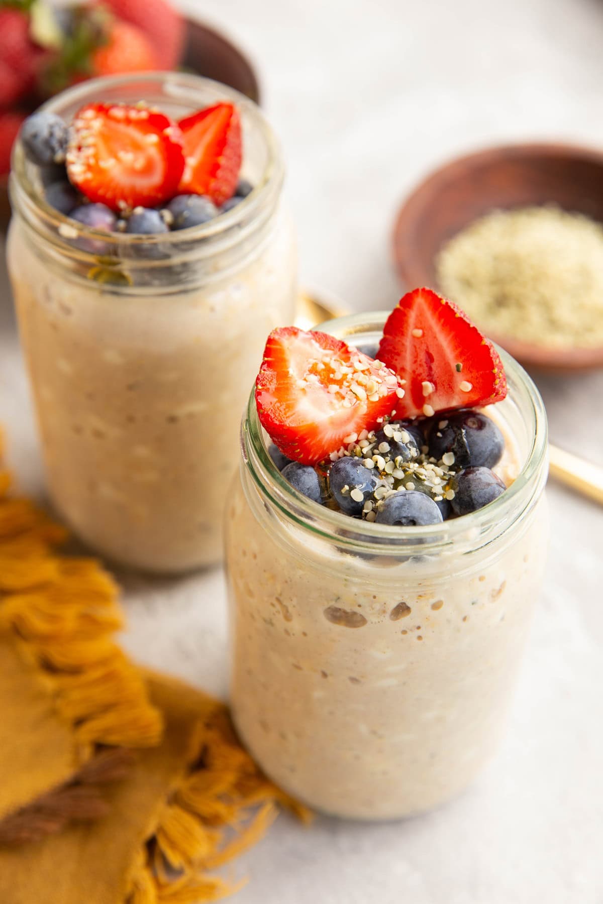 Two jars filled with cottage cheese overnight oats with fresh blueberries, chopped strawberries and honey on top.