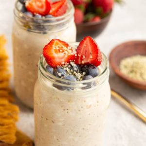 Two jars full of cottage cheese overnight oats with fresh fruit on top and a bowl of strawberries in the background.