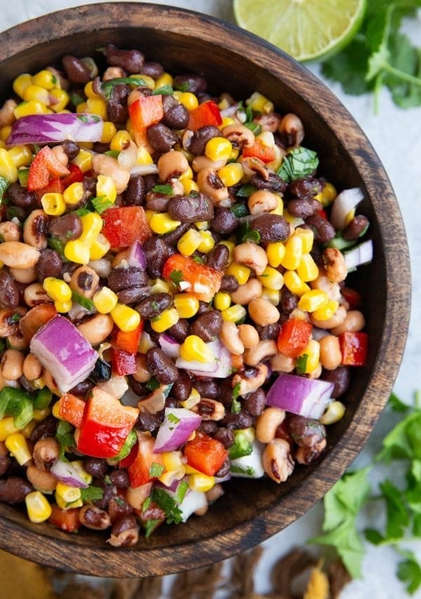 Cowboy caviar inside of a wooden bowl with fresh cilantro to the side.