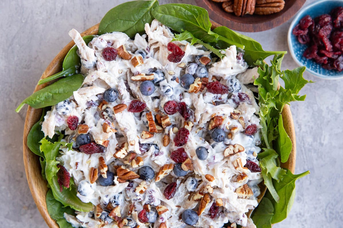 Chicken salad in a wooden bowl with fresh greens to the side, ready to eat.