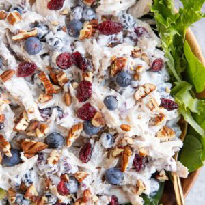 large wooden bowl full of chicken salad on a bed of lettuce.