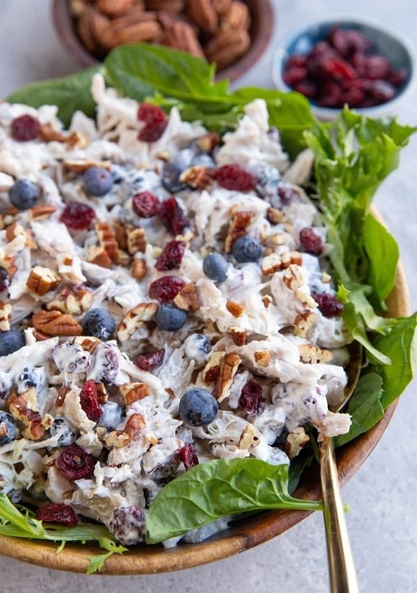 Wooden bowl full of chicken salad with a golden spoon for scooping.