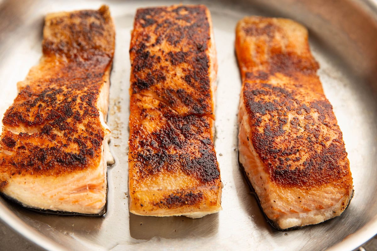 Stainless steel skillet with three large salmon fillets