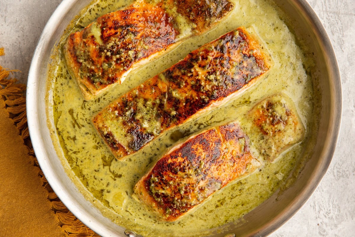 Stainless steel skillet with seared salmon and creamy pesto sauce.