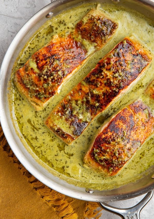 Crispy salmon in a skillet with creamy pesto sauce