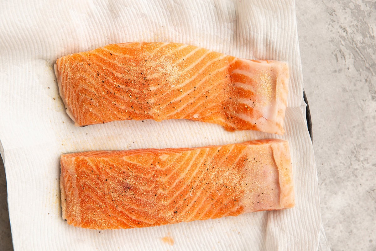 Raw salmon fillets on a plate with a paper towel.