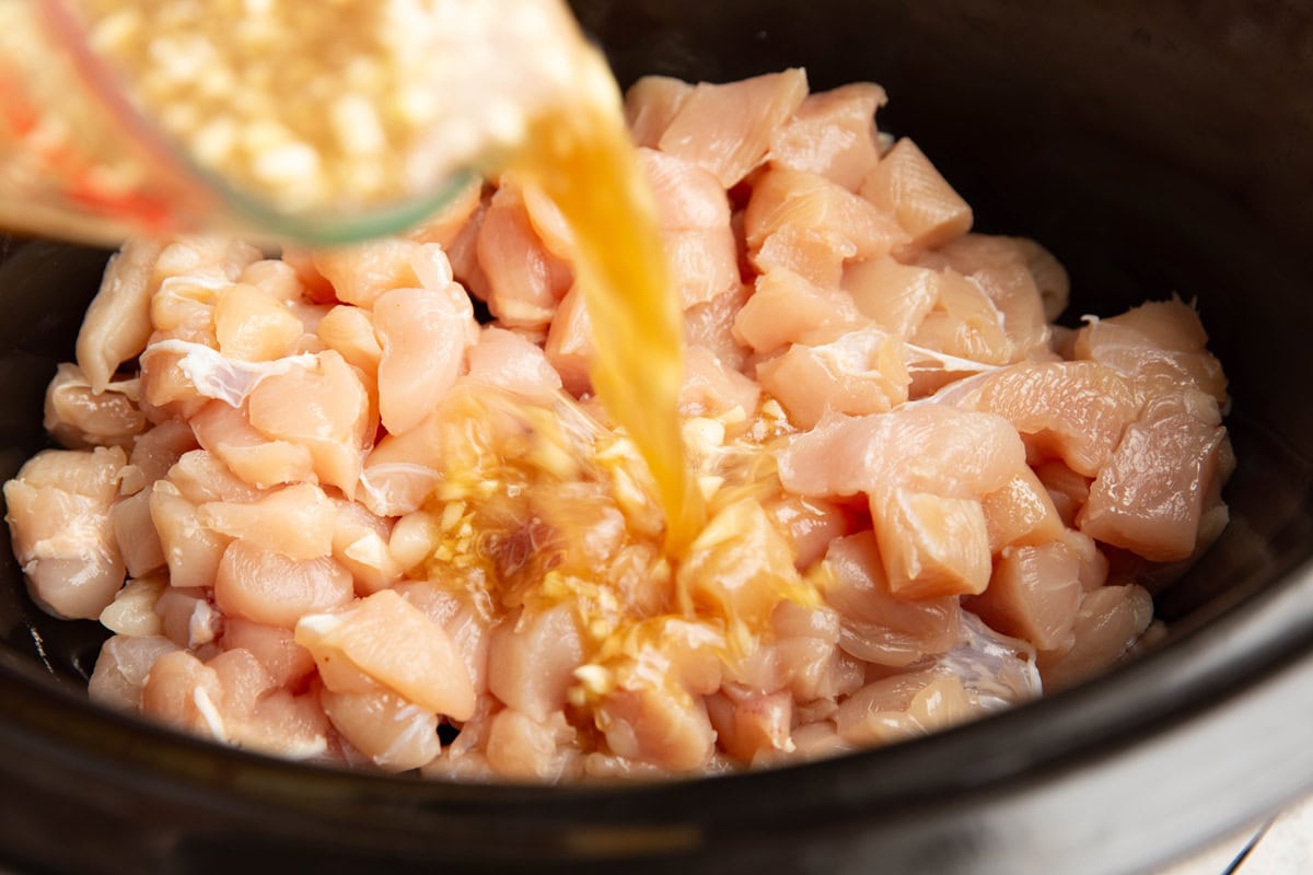 Pouring the sauce into the slow cooker from a measuring cup into the chopped chicken.