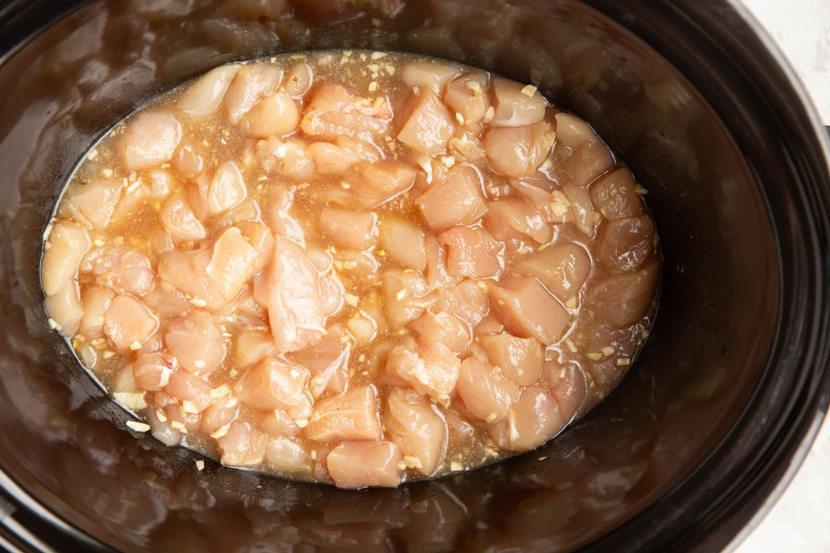 Slow cooker filled with chopped chicken and sauce.