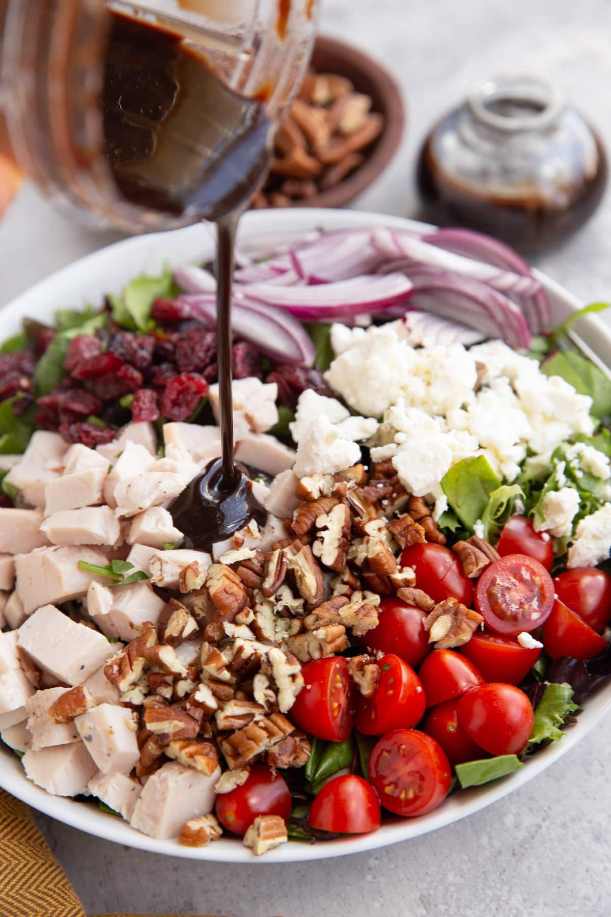 Pouring balsamic dressing over salad in a large salad bowl.