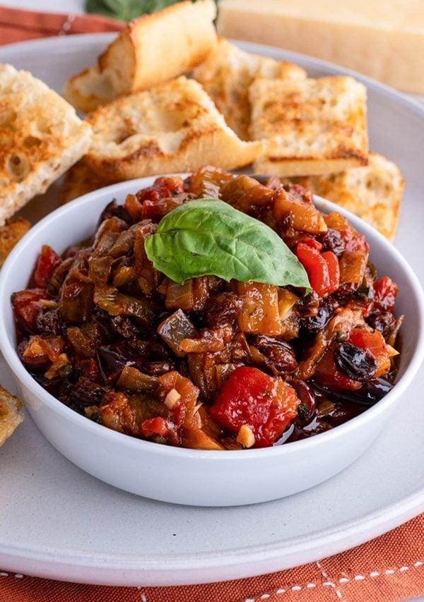 bowl of eggplant caponata with toasted bread on a plate, ready to serve.