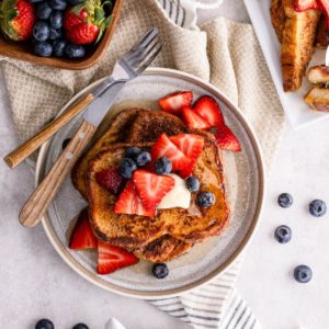 Plate of French toast with a bowl of fresh blueberries and strawberries to the side.