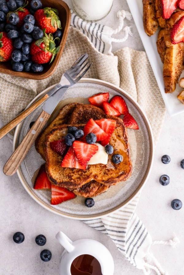 Plate of French toast with a bowl of fresh blueberries and strawberries to the side.