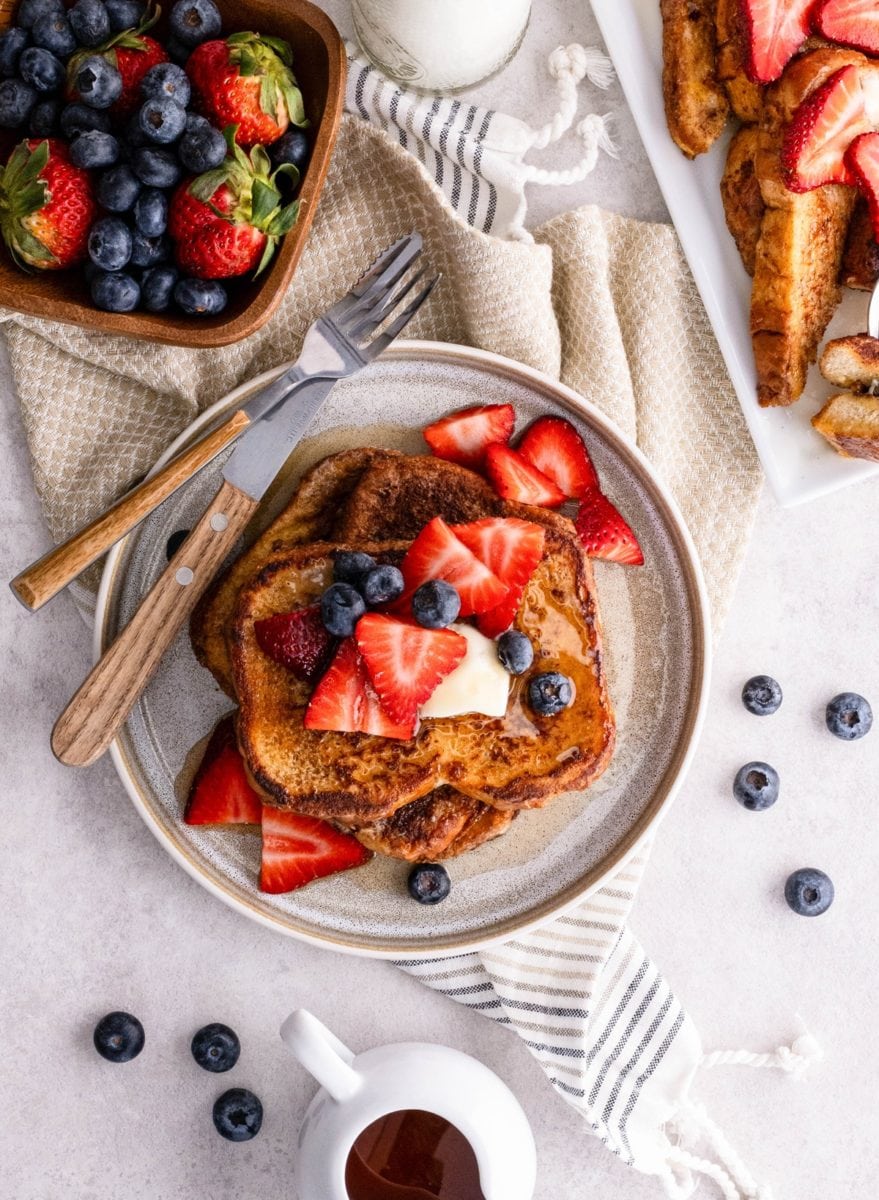 Plate of French toast with a bowl of fresh blueberries and strawberries to the side.