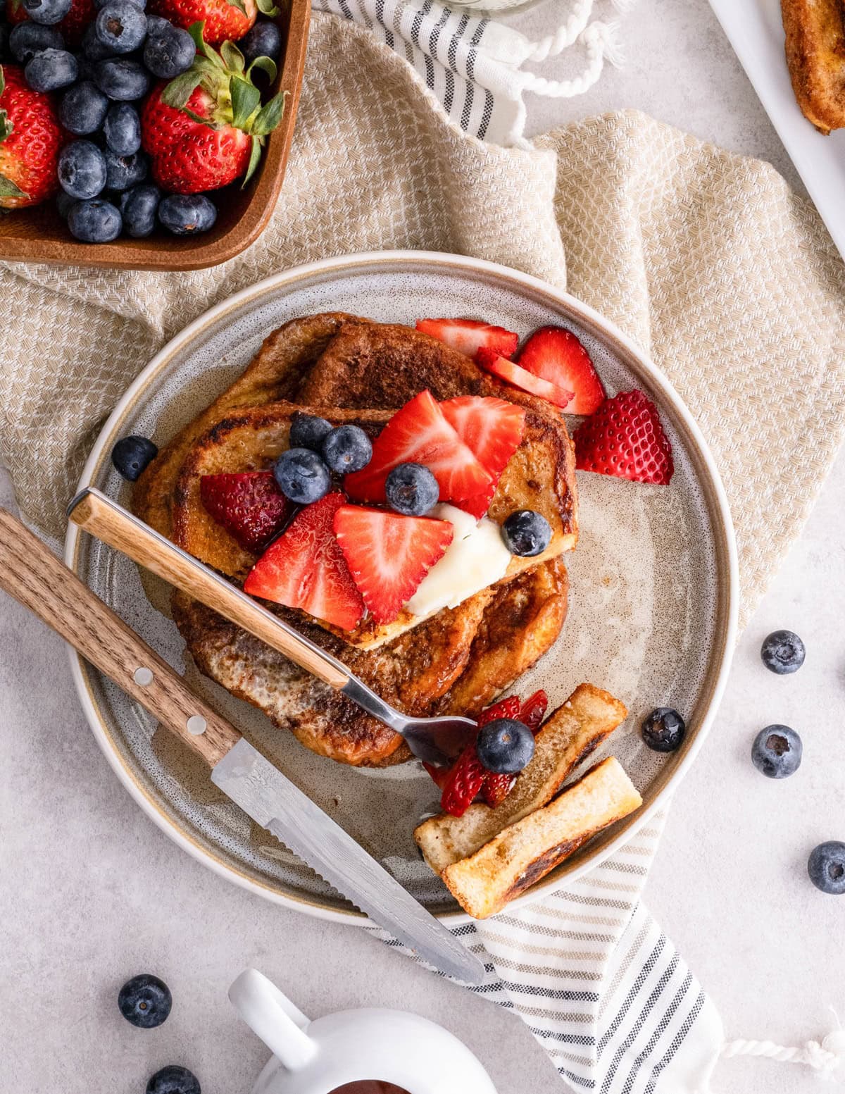Stack of berry covered toast on a plate with a bite taken out.